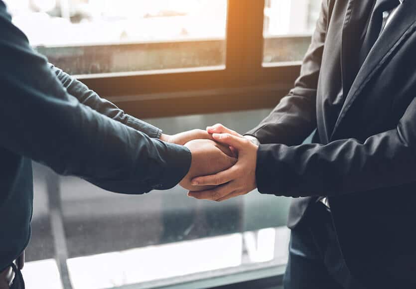 Két személy fogja a másik kezét, mindkét kezükkel megszorítva a másik személy mindkét kezét.